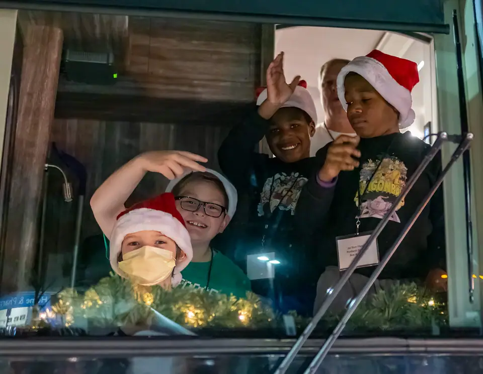 Kids in Santa hats peeking out of a bus windshield at night