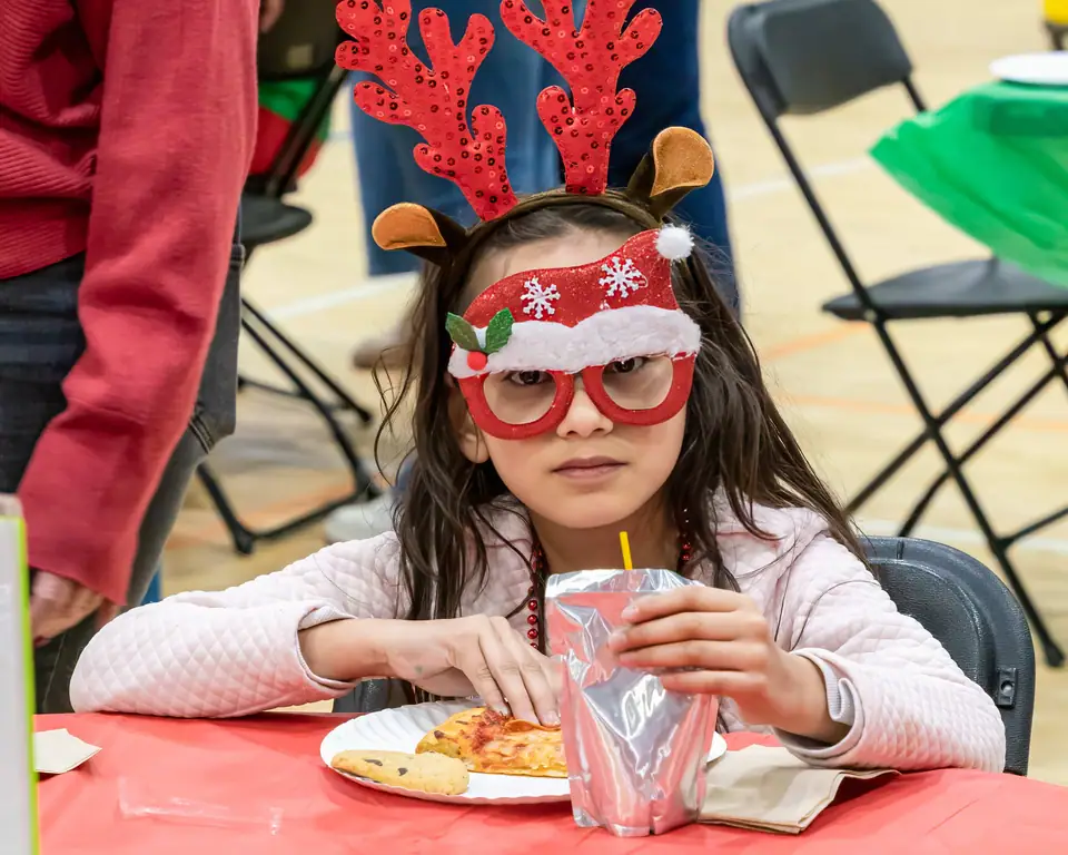 A girl in reindeer antlers and Christmas glasses at her party table