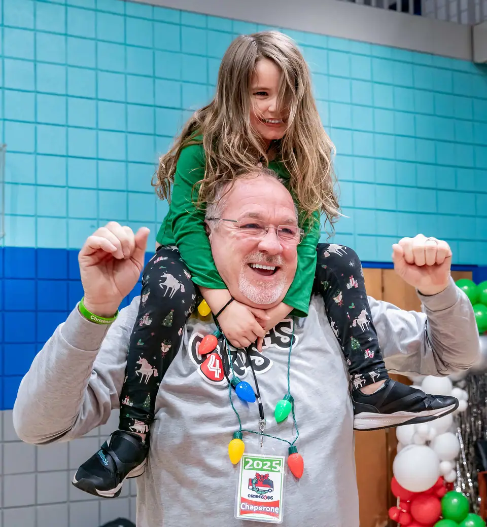 A volunteer carrying a laughing kid on his shoulders