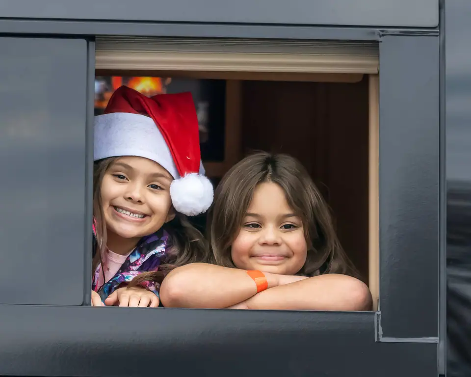 Two girls, one in a Santa hat, smiling out of a tour bus window