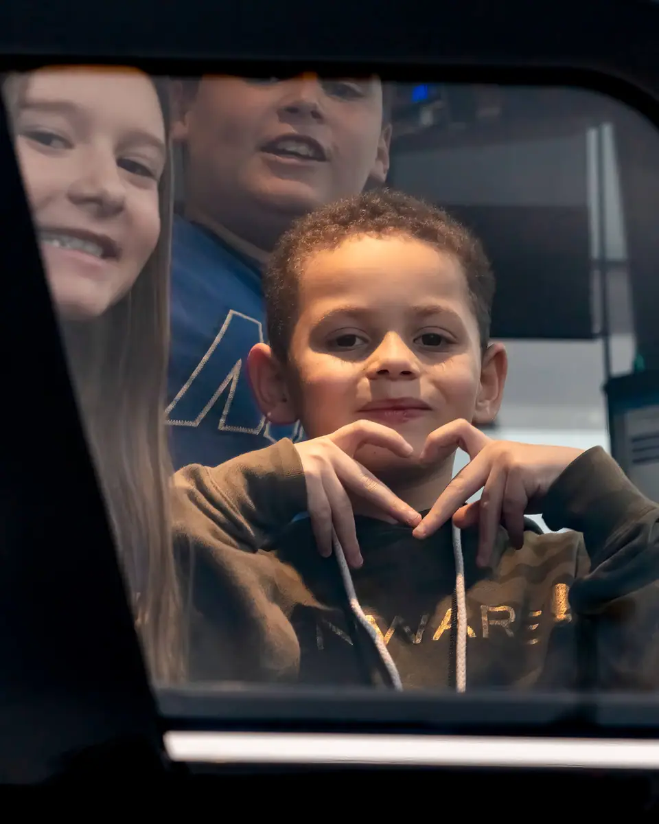 A boy making a heart with his hands through a tour bus window