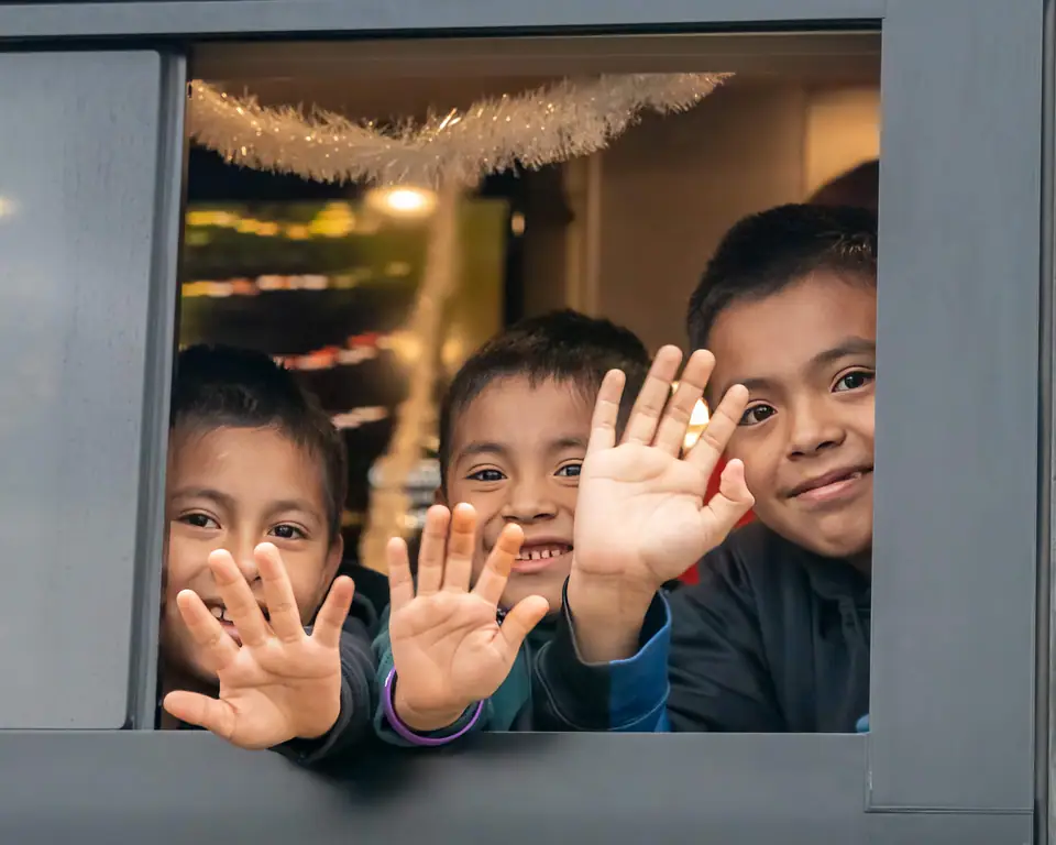 Kids pressing their hands to a tour bus window and waving