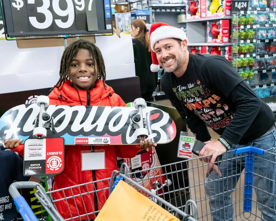 A boy with a cart full of boxes beside his chaperone in a Santa hat